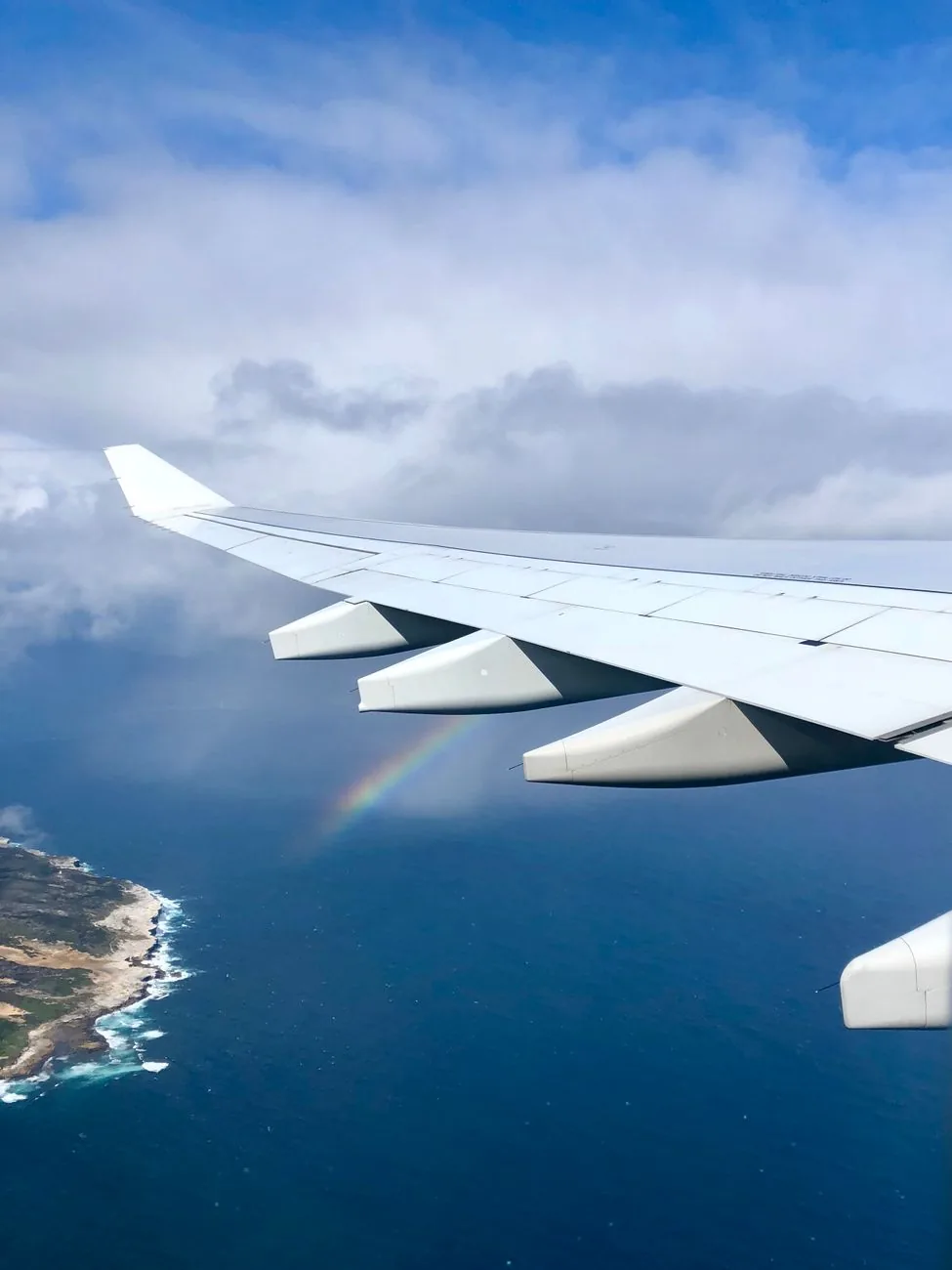 Aile d'avion au-dessus d'une côte, arc-en-ciel en contrebas