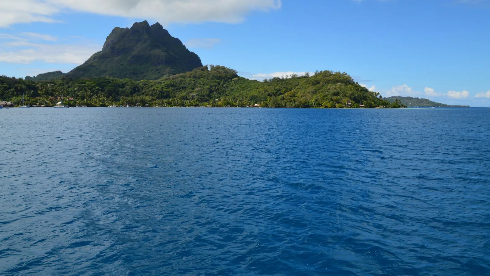Relief de Bora Bora vu depuis le chenal du lagon, voiliers au mouillage le long de la côte