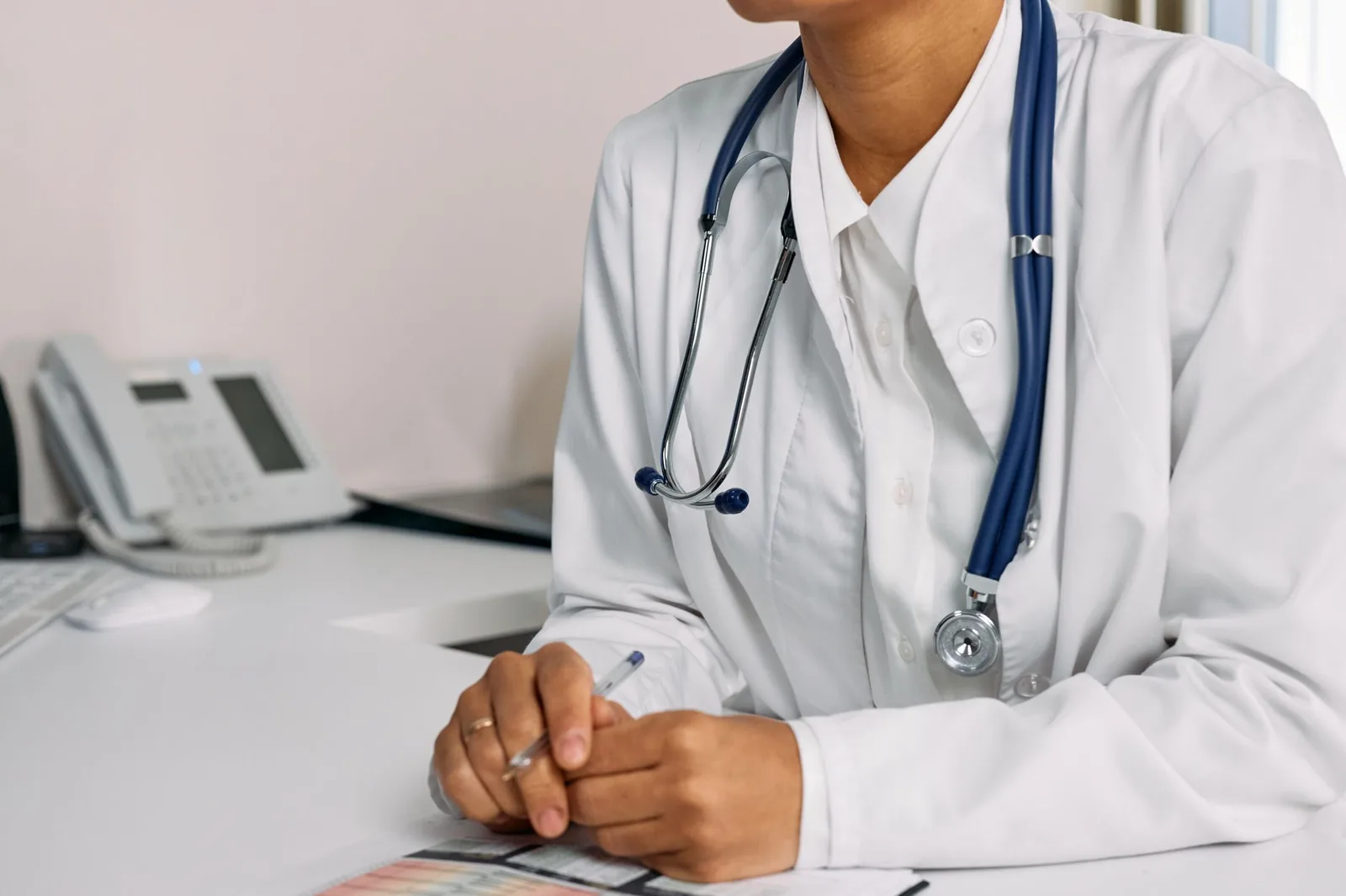 Médecin en blouse blanche, stéthoscope autour du cou, assis à son bureau de consultation