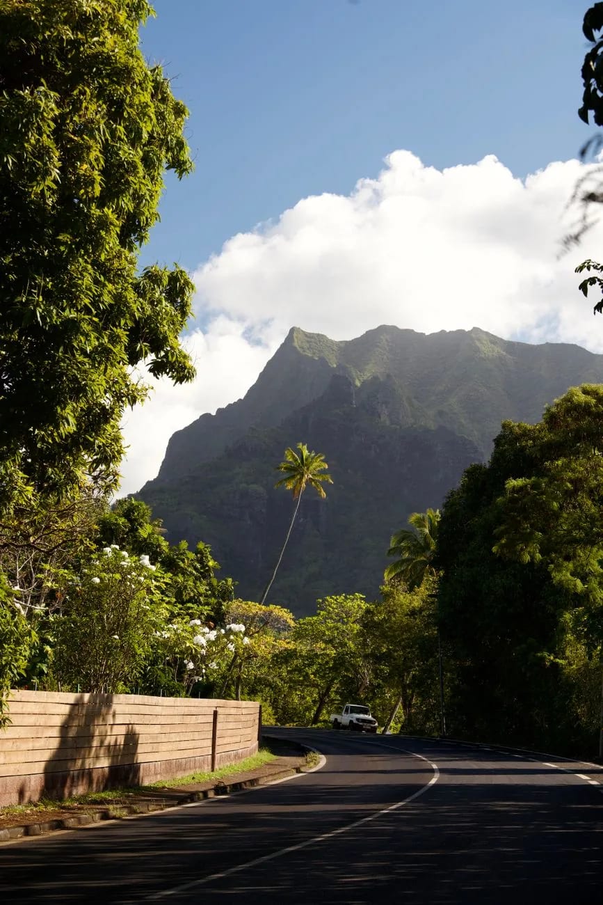 Route goudronnée de Moorea bordée de végétation, un pick-up au pied des reliefs volcaniques