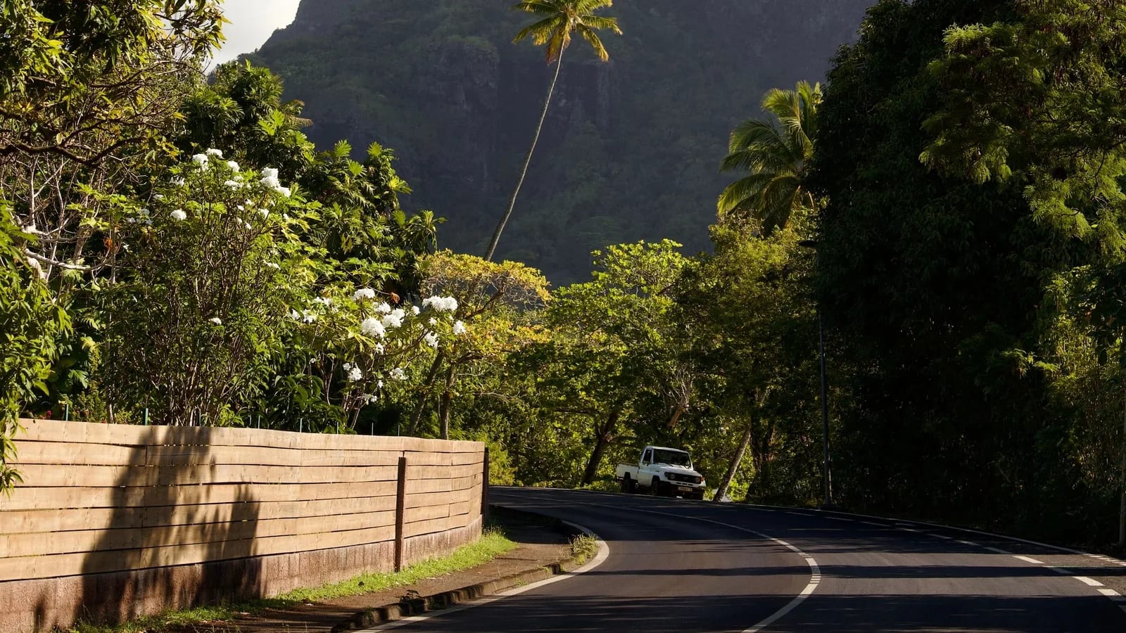 Route côtière goudronnée en Polynésie française, un pick-up au pied des reliefs volcaniques