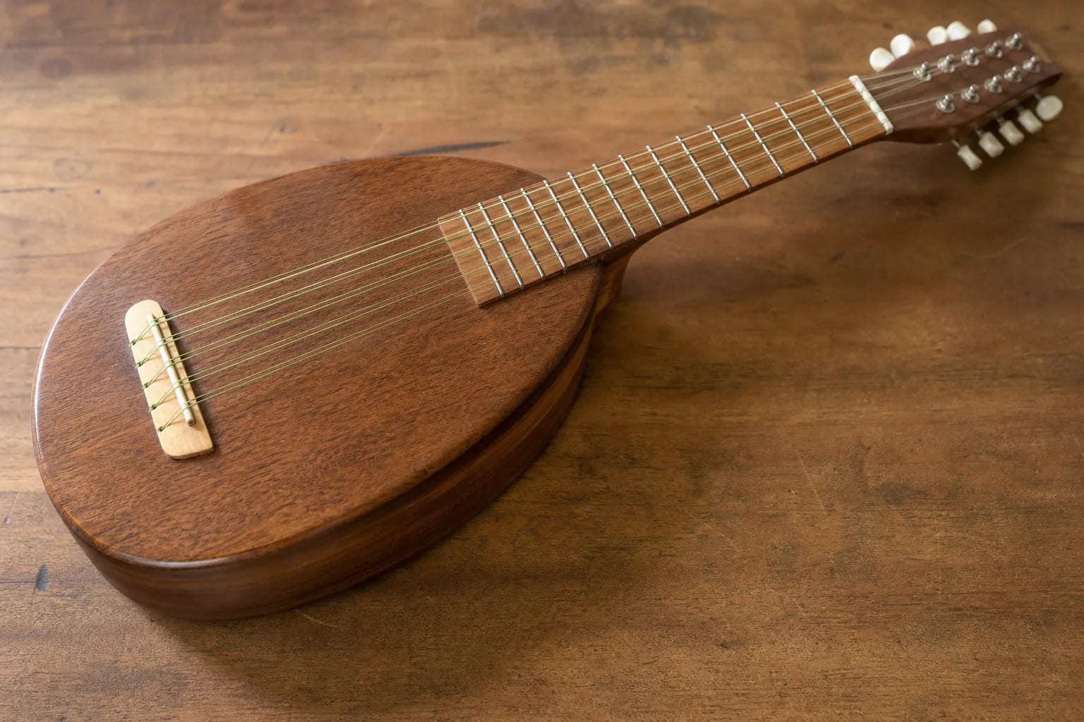 Gros plan d'un ukulele tahitien en bois massif brun, sans rosace, chevalet sur une fine planche claire, huit cordes en quatre paires (illustration)